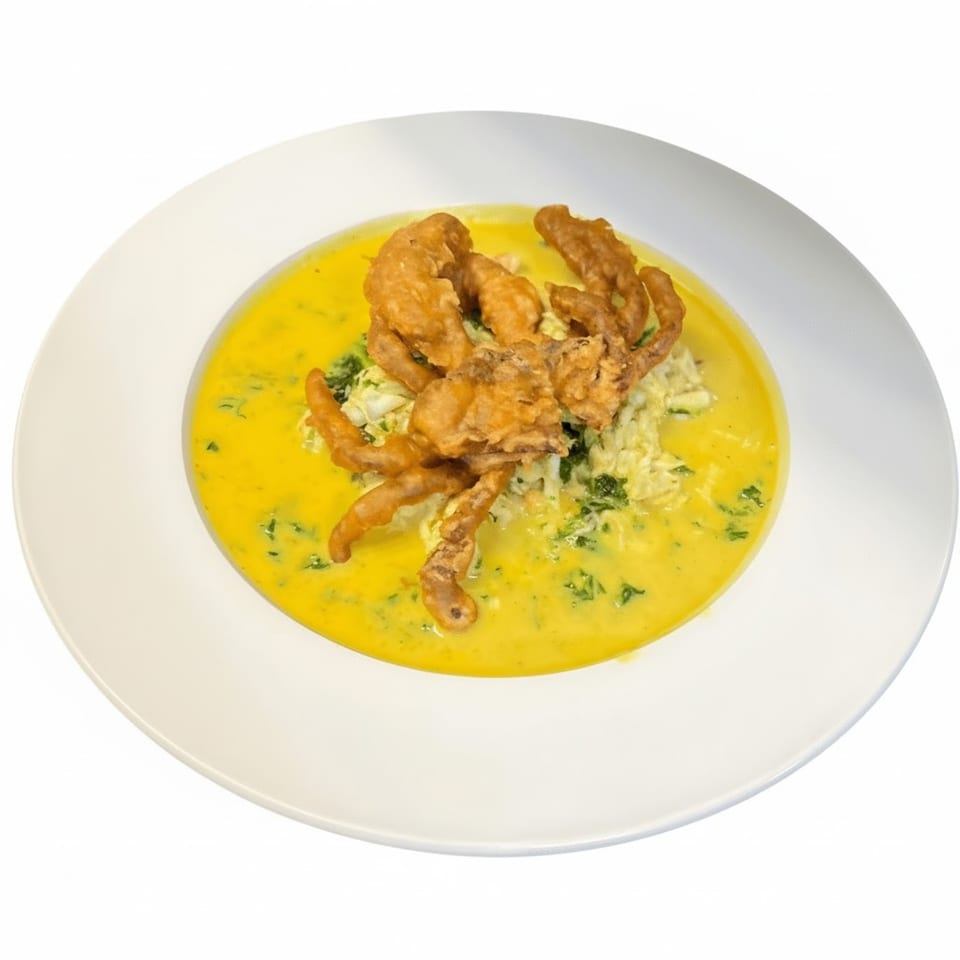 Crispy fried soft-shell crab served in a yellow curry sauce with herbs, a Thai dish.