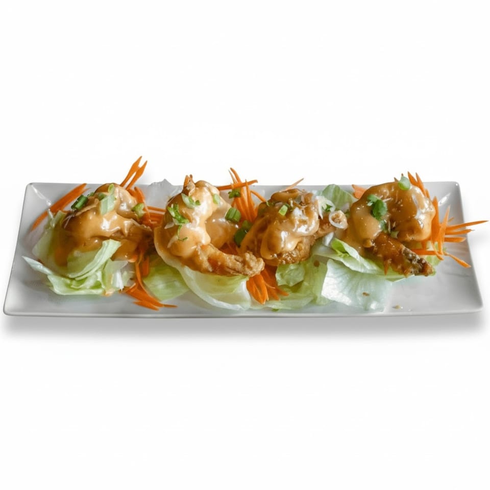 Four crispy shrimp appetizers topped with creamy sauce, green onions, and shredded carrots on lettuce.