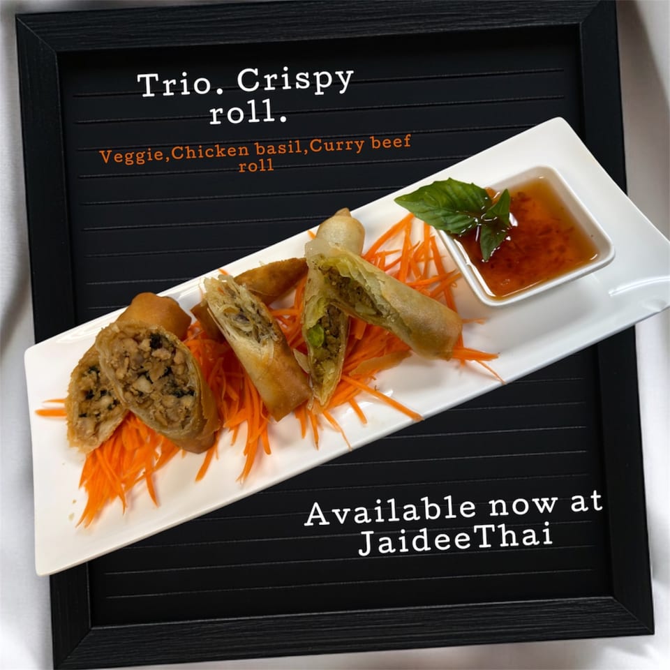 Crispy spring rolls with various fillings, shredded carrots, and a dipping sauce with basil on a white plate.
