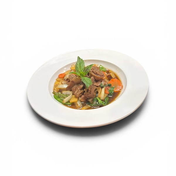 Beef stir-fry with carrots, onions, and green vegetables, garnished with basil, in a white bowl.