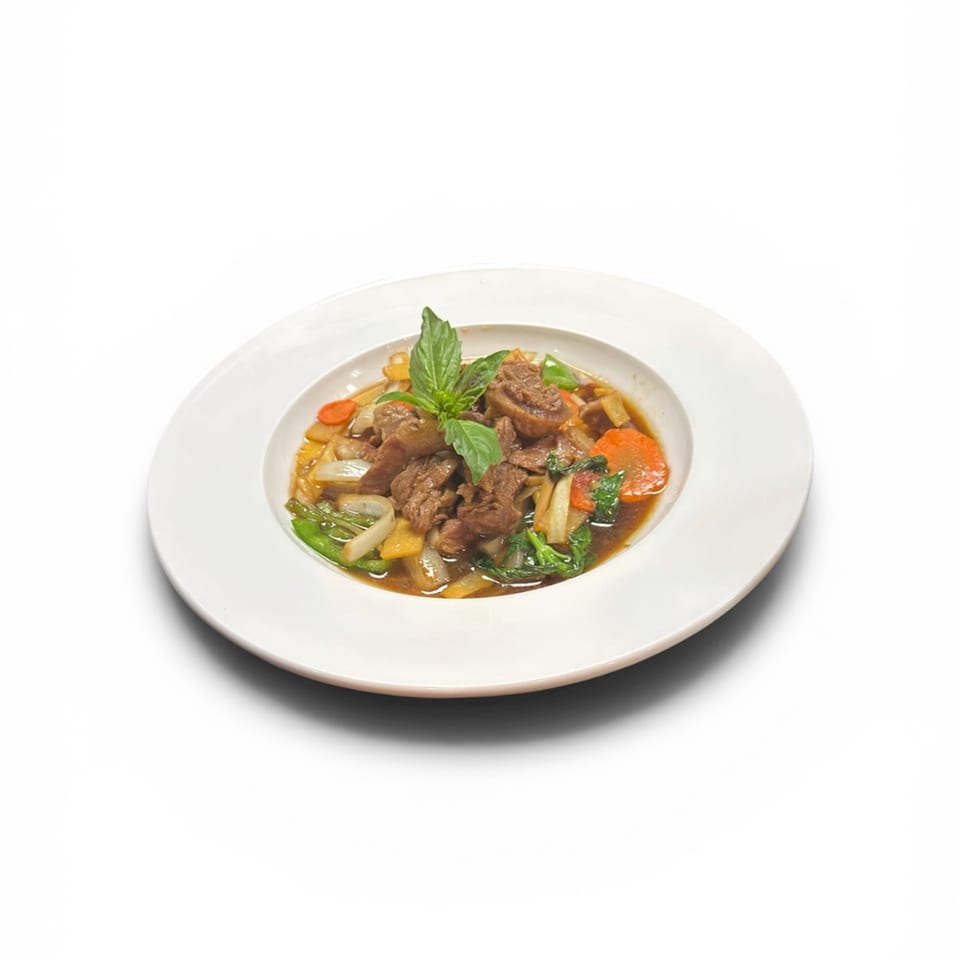 Beef stir-fry with carrots, onions, and green vegetables, garnished with basil, in a white bowl.